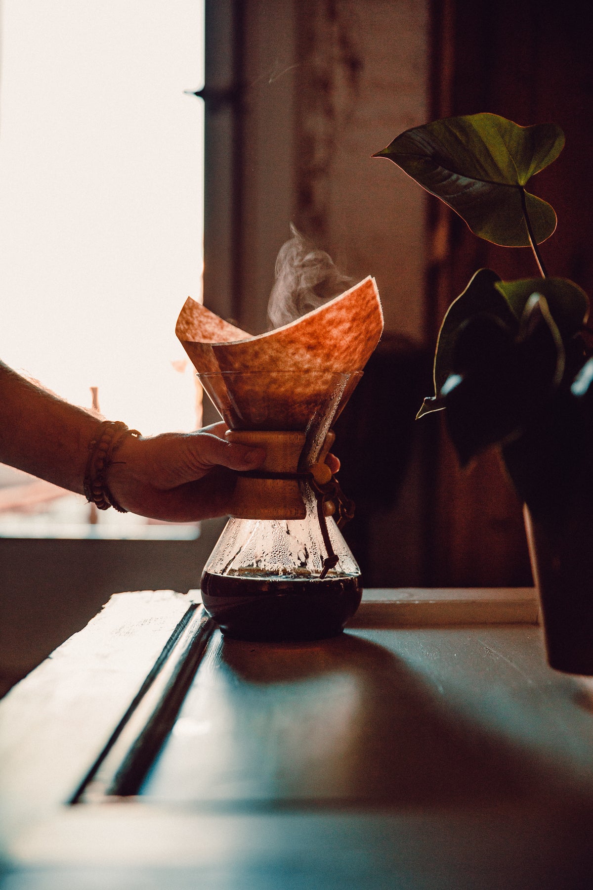 Hand lifting a steaming Chemex of freshly brewed kosher coffee